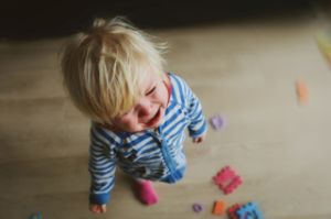 Ein kleiner Junge steht weinend im Zimmer neben seinem Spielzeug.