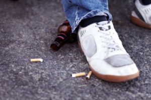 Ein Fuß auf dem Boden neben Zigarettenstummel und einer Bierflasche.