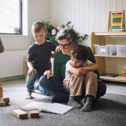 Erzieherin liest zwei Kindern ein Buch auf dem Boden vor.