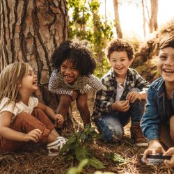 Kinder sitzen lachend zusammen im Wald.