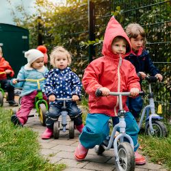 Mehrere Kinder aus der Kita bewegen sich in einer Reihe mit Laufrädern fort.