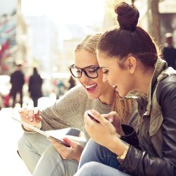 Zwei Frauen sitzen mit einem Tablet in der Hand an der Straße.