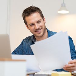 Mann sitzt am Schreibtisch und schaut auf ein Blatt Papier in seiner Hand.
