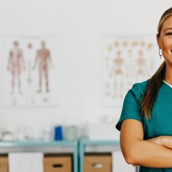 Eine junge Frau in grüner, medizinischer Kleidung steht in einem Sprechzimmer einer Physiotherapie-Praxis.