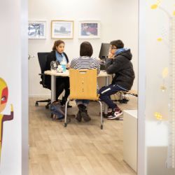 Zwei Erwachsene und ein Teenager sitzen in einem Büro an einem runden Tisch.