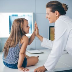 Aerztin gibt einem Mädchen in der Praxis auf dem Behandlungsbett ein high five.