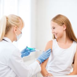 Ärztin gibt jungem Mädchen eine Spritze in den Oberarm.