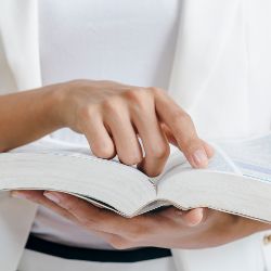 Eine Frau hält ein Buch in der Hand und zeigt mit einem Finger auf eine Stelle.