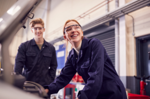Junge und Mädchen stehen in Autowerkstatt vor Wagen mit geöffneter Motorhaube.