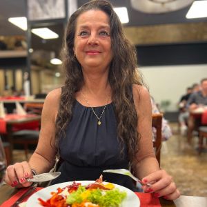 Frau sitzt im Restaurant mit einem Teller vor sich und lächelt zufrieden. 