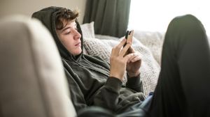 Jugendlicher sitzt auf dem Sofa und tippt am Handy.