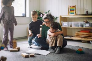 Erzieherin liest zwei Kindern ein Buch auf dem Boden vor.