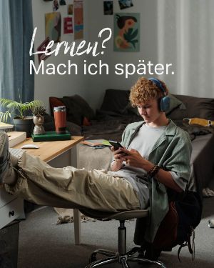"Lernen? Mach ich später." Ein junger Mann sitzt am Schreibtisch aber spielt am Handy.