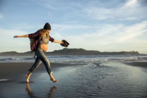 Eine Schwangere springt am Strand durch das Wasser und freut sich.