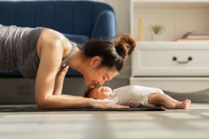 Eine Frau macht Sport auf Yogamatte und ist über Ihr Baby gebeugt