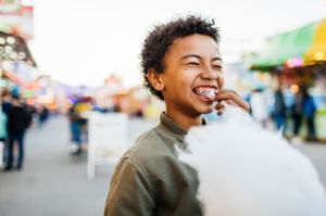 Ein Junge mit einer Zahnspange im Mund isst Zuckerwatte und lacht.