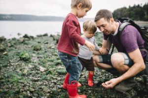 Ein Vater zeigt seinen Kindern etwas am Steinstrand.