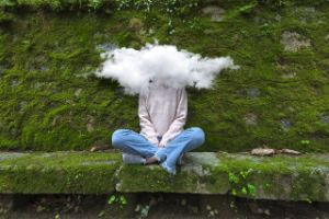 Jugendliche sitz vor einer mit Moss bedeckten Mauer und hat eine Wolke um den Kopf.