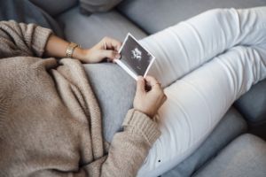 Eine schwangere sitzt auf einer Couch und hält ein Ultraschallbild in den Händen.