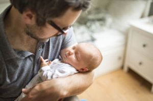 Mann mit Brille hält schlafendes Baby im Arm.