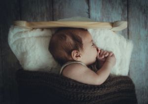 Baby schläft mit Daumen im Mund im Babybett.