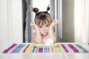 Kleines Mädchen sitzt verzweifelt mit den Händen am Kopf vor einer Milchspeise.