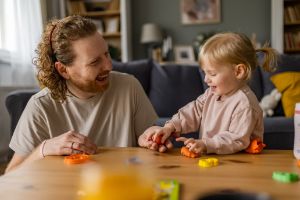 Vater und Kleinkind spielen und unterhalten sich, beide lachen, das Bild steht für Sprachentwicklung.