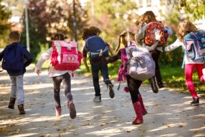 Grundschulkinder mit Schulranzen rennen draußen auf einem Weg und sind von hinten zu sehen.
