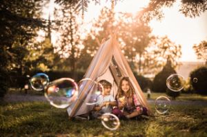 Im Garten sitzen zwei Kinder bei Sonnenuntergang im Zelt und pusten Seifenblasen.