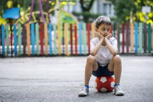 Junge sitzt auf rotem Ball, er sieht alleine und traurig aus.