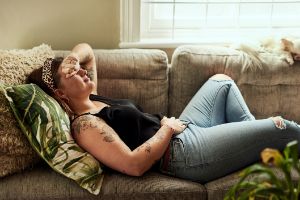 Eine Frau liegt auf der Couch und hält sich vor Schmerzen den Bauch.