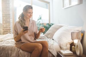 Eine Frau sitzt auf einem Bett und hält Tabletten in Ihrer Hand.