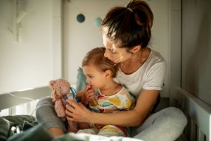 Eine Mutter sitzt mit ihrem kranken Kind im Bett und verarzten einen kleinen Teddybär.