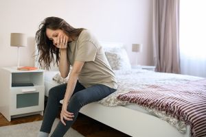 Schwangere sitzt auf Bett, stützt sich auf Knie ab und hält Hand vor den Mund.
