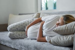 Schwangere liegt lang auf Sofa, hält ihren Bauch, ihr gehts schlecht, ist müde.