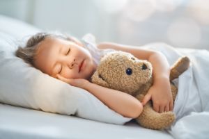 Kind schläft mit Teddy im Bett.