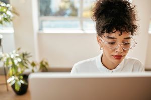 Junge Frau mit Kurzsichtigkeit sitzt mit Brille vor ihrem Laptop.