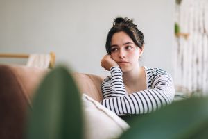 Junge Frau mit Depressionen sitzt betrübt auf der Couch.