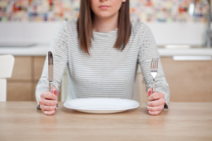 Eine Frau sitzt vor einem leeren Teller und ist wütend vor Hunger.