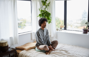 Ein junger Mann sitzt meditierend auf seinem Bett.