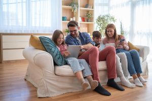 Eltern spielen lachend mit ihren 2 kleinen Kindern auf dem Sofa mit Holzspielzeug.