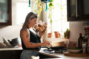Eine übergewichtige Frau schaut aufs Handy und kocht.