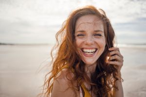 Frau am Strand, ihr Gesicht ist abgebildet und sie hat ein strahlendes Lachen.