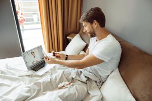 Ein Mann sitzt krank im Bett und telefoniert per Video mit einem Arzt.