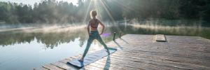 Eine Frau macht morgens am See Yoga auf einem Steg.