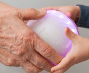 Hand eines Senioren und Hand eines Kindes umfassen den Ichó Therapieball. 
