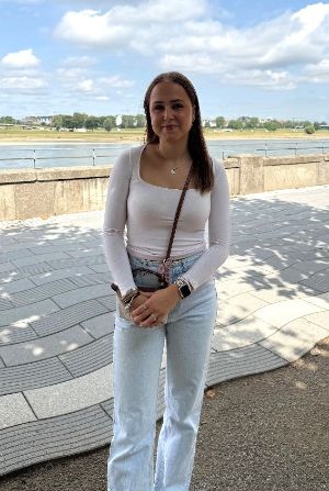 Ein junges Mädchen steht vor einem Fluss und lächelt in die Kamera.