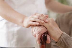 Eine Pflegerin hält die Hand eines alten Menschen mit Gehstock.