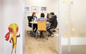 Zwei Erwachsene und ein Teenager sitzen in einem Büro an einem runden Tisch.