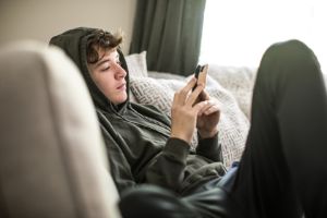 Junge sitzt traurig vor seinem Handy. 